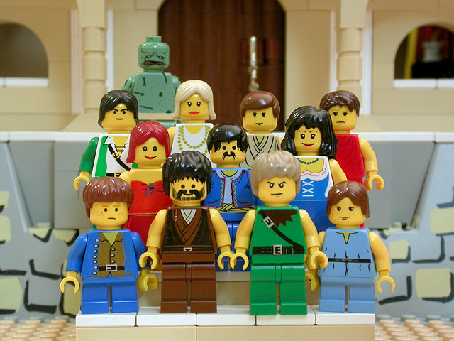 In an image from the Brick Testament, a webpage with Bible stories enacted in Lego toys.  This image is of Job 42:13 the restoration of job's family with 7 sons and 3 daughters.  They are standing, arranged on the steps of a grand house, in rows, facing the imagined camera. Job is still afflicted by the skin disease and appears green and scaly (in the upper left).