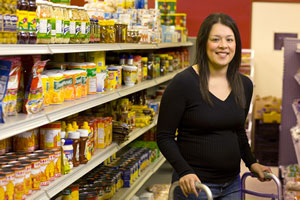 Patty stands in a grocery aisle.  She is wearing black and has a walker.  She is looking directly into the camera with a broad smile.