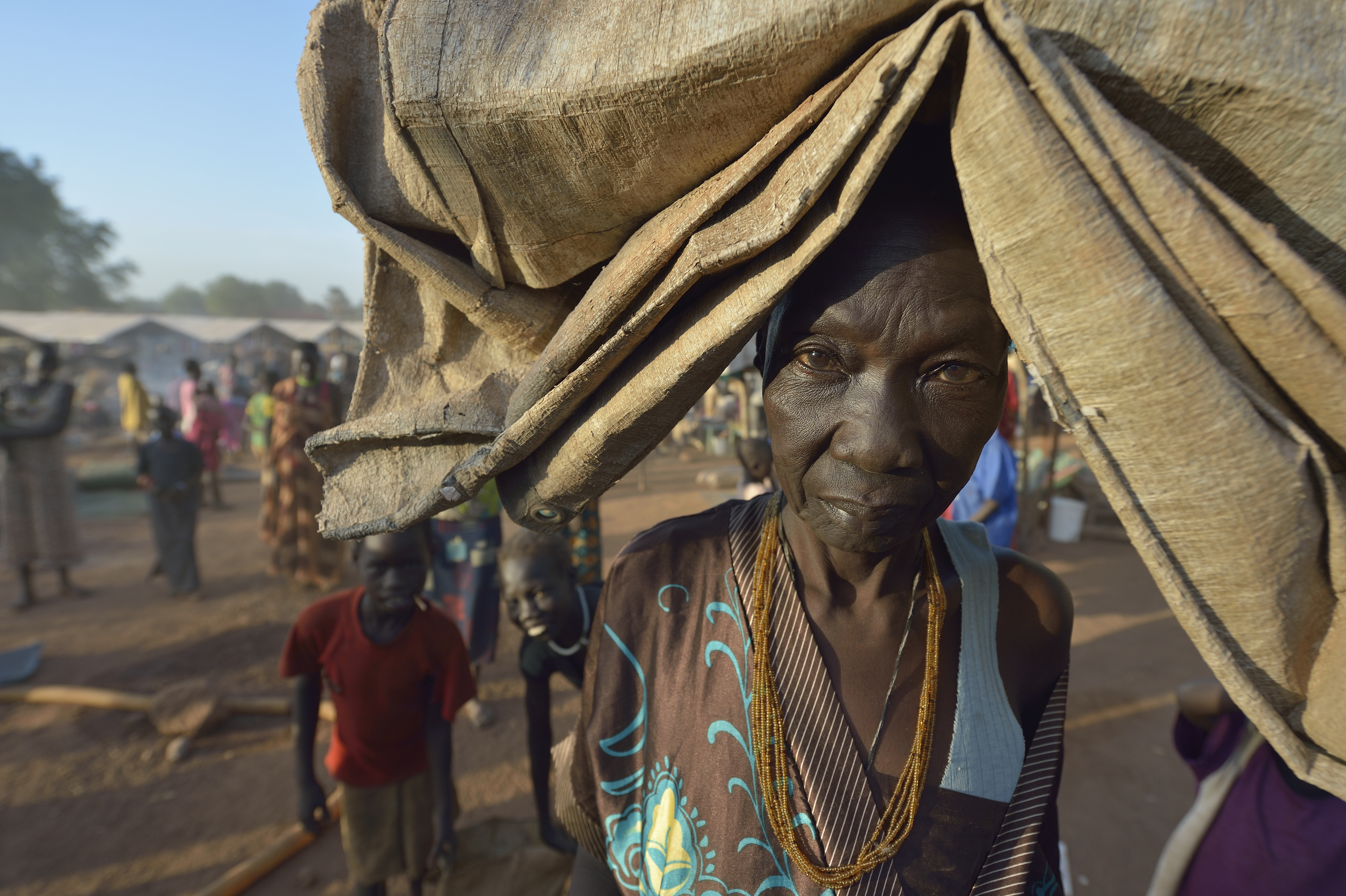 A woman carries her tarp early in the morning in a camp for over 5,000 internally displaced persons in an Episcopal Church compound in Wau, South Sudan. Most of the families here were displaced by violence early in 2017, after a larger number took refuge in other church sites when widespread armed conflict engulfed Wau in June 2016. Most of the people in this camp have no shelter, and use a tarp or mats to lay on the ground at night.